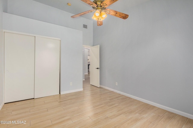 unfurnished bedroom featuring ceiling fan, a towering ceiling, a closet, and light wood-type flooring