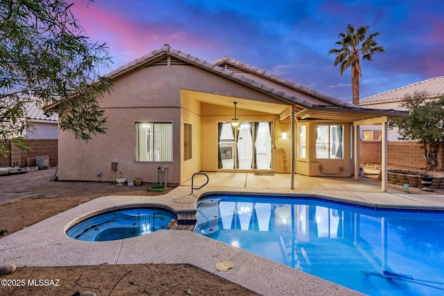 pool at dusk featuring an in ground hot tub, ceiling fan, and a patio area