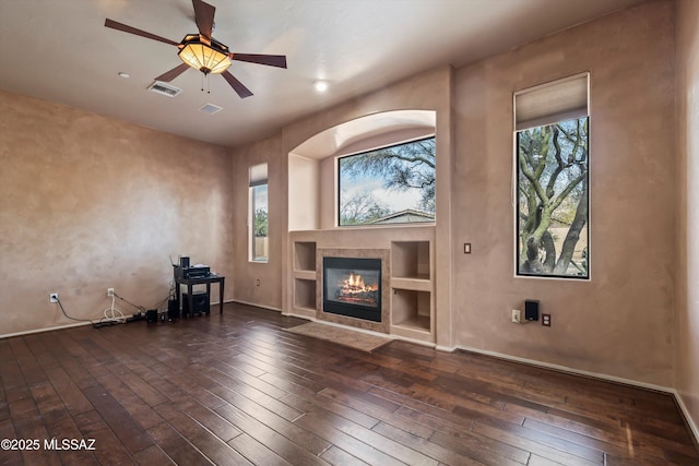 unfurnished living room featuring a tiled fireplace, dark hardwood / wood-style floors, ceiling fan, and built in shelves