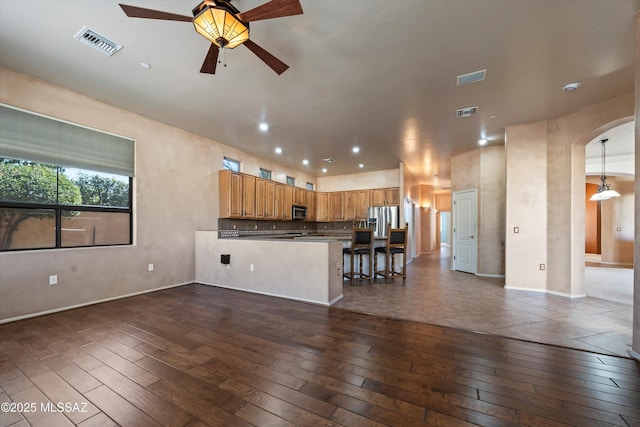 kitchen featuring a breakfast bar area, appliances with stainless steel finishes, dark hardwood / wood-style floors, kitchen peninsula, and pendant lighting