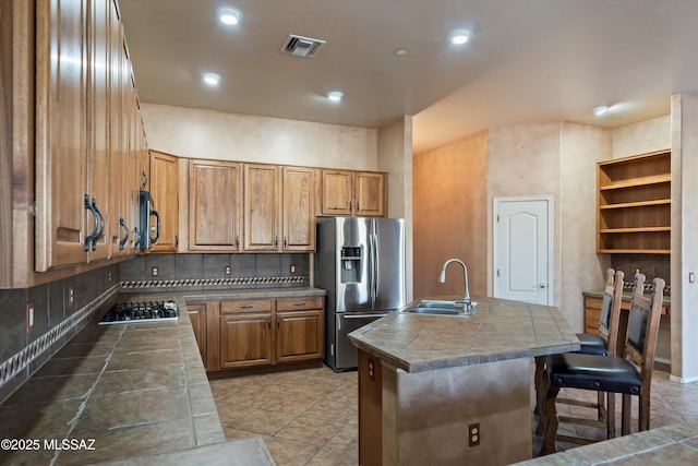 kitchen with tile countertops, tasteful backsplash, an island with sink, sink, and stainless steel appliances