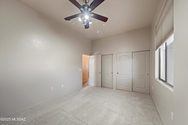 unfurnished bedroom featuring light carpet, two closets, and ceiling fan