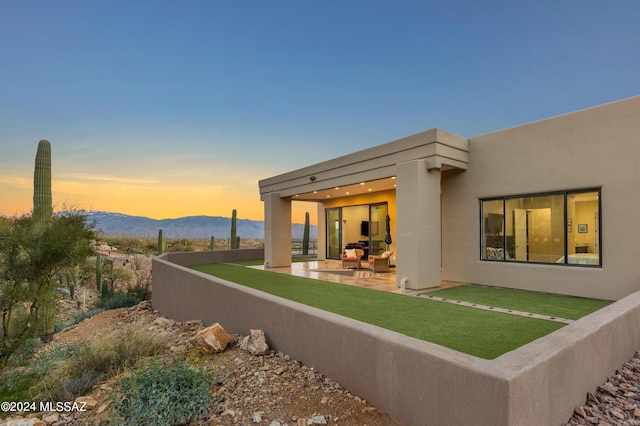 back house at dusk featuring a mountain view, a yard, and a patio