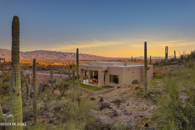 back house at dusk with a mountain view and a patio area