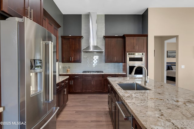 kitchen with wall chimney exhaust hood, sink, tasteful backsplash, appliances with stainless steel finishes, and light hardwood / wood-style floors