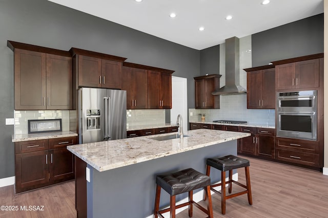 kitchen with sink, a center island with sink, wall chimney exhaust hood, and appliances with stainless steel finishes