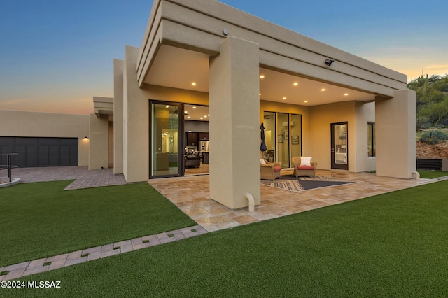 back house at dusk featuring a yard and a patio area