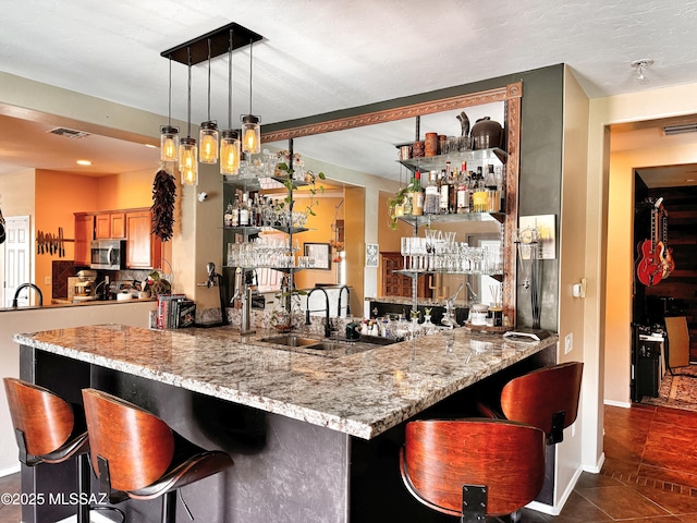 bar with sink, hanging light fixtures, dark tile patterned floors, and light stone counters