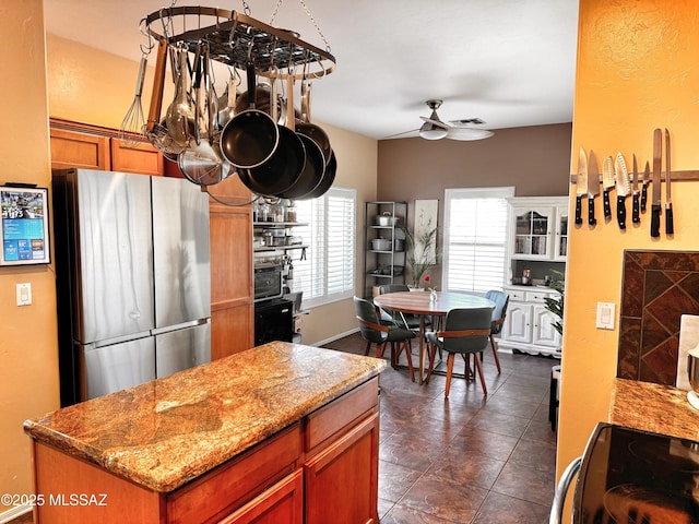 kitchen featuring light stone counters, a center island, range with electric cooktop, ceiling fan, and stainless steel refrigerator