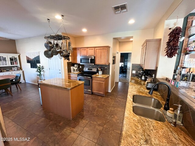 kitchen featuring sink, appliances with stainless steel finishes, a center island, and light stone counters