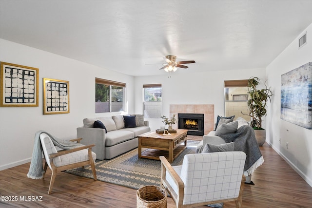 living room with a tiled fireplace, dark hardwood / wood-style floors, and ceiling fan