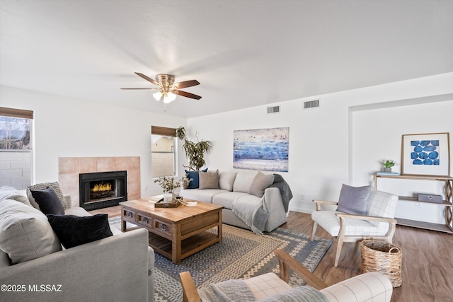 living room featuring ceiling fan, wood-type flooring, and a tiled fireplace