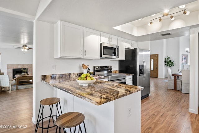 kitchen with stainless steel appliances, white cabinets, kitchen peninsula, dark stone counters, and light wood-type flooring