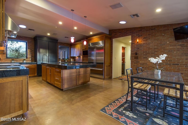 kitchen with brick wall, visible vents, hanging light fixtures, a center island, and stainless steel built in refrigerator