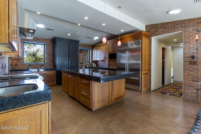 kitchen with built in appliances, brick wall, visible vents, hanging light fixtures, and an island with sink