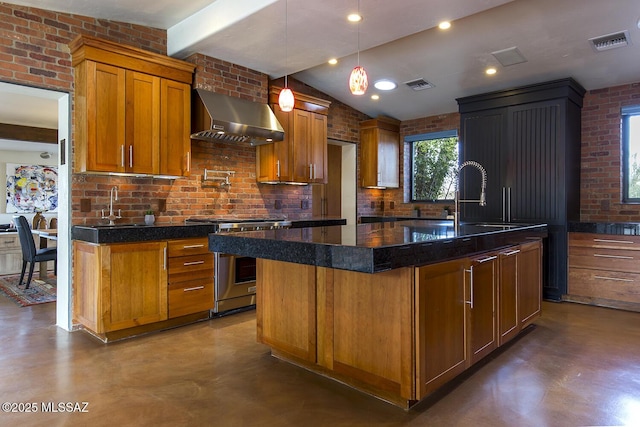 kitchen featuring visible vents, brick wall, wall chimney exhaust hood, a kitchen island with sink, and stainless steel stove