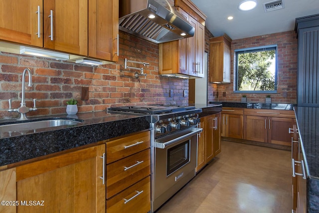 kitchen with a sink, visible vents, wall chimney range hood, stainless steel range, and dark stone countertops