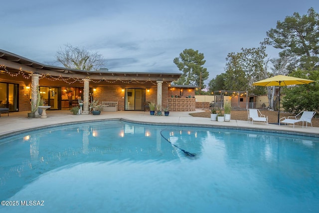 pool at dusk with an outdoor pool and fence