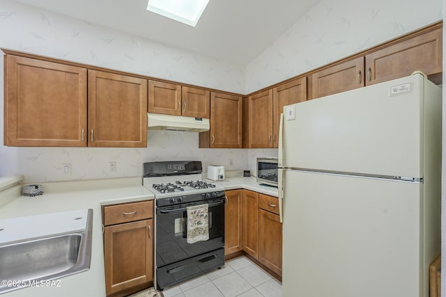 kitchen featuring sink, vaulted ceiling with skylight, gas stove, light tile patterned flooring, and white fridge