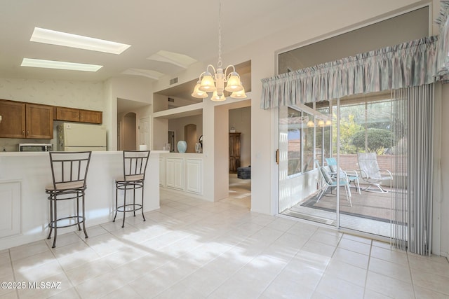 kitchen featuring lofted ceiling, hanging light fixtures, a kitchen breakfast bar, white refrigerator, and a chandelier