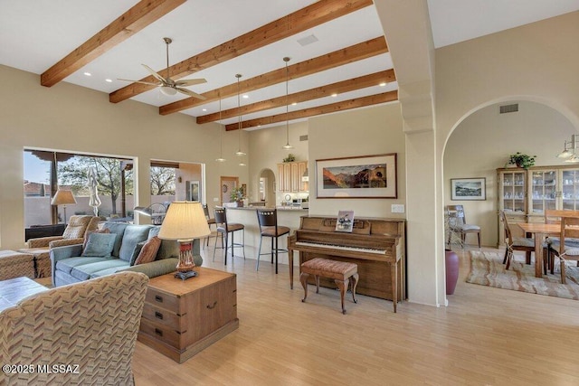 living room featuring a high ceiling, ceiling fan, light hardwood / wood-style floors, and beamed ceiling