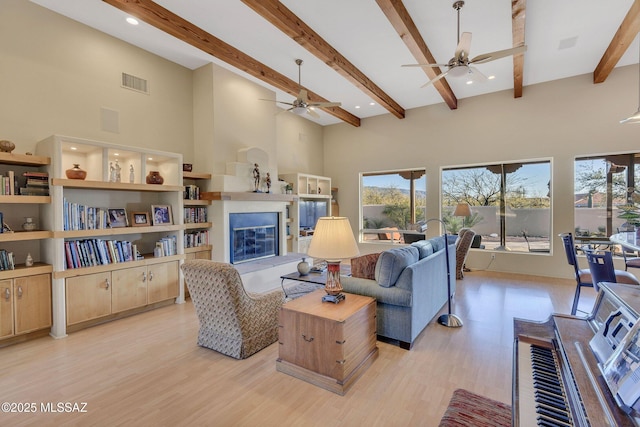 living room with beam ceiling, light hardwood / wood-style floors, ceiling fan, and a high ceiling