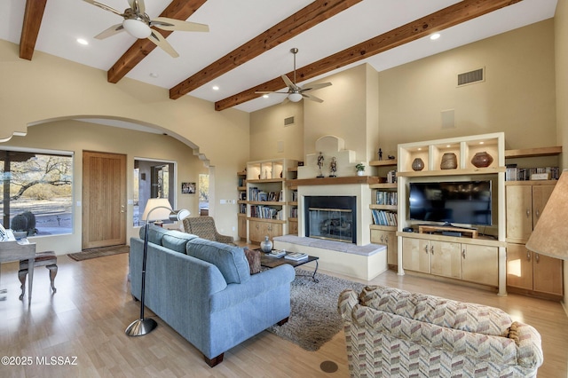 living room featuring a fireplace, light hardwood / wood-style flooring, ceiling fan, and a high ceiling