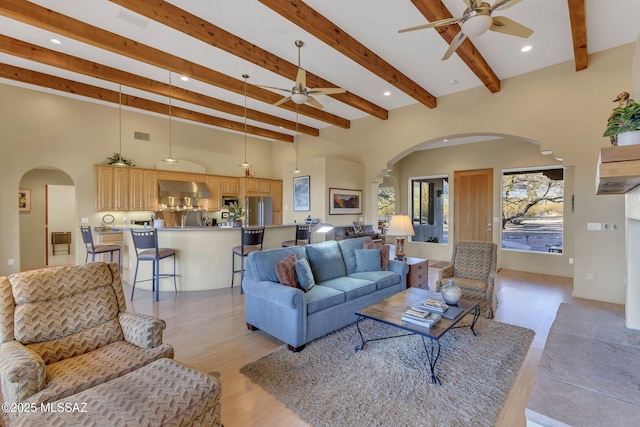 living room with ceiling fan, a towering ceiling, and beam ceiling