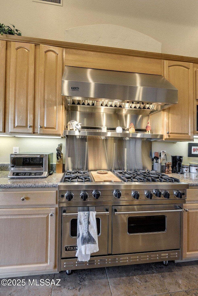 kitchen featuring light stone counters, ventilation hood, range with two ovens, and light brown cabinets