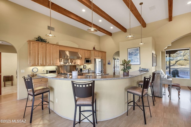 kitchen featuring appliances with stainless steel finishes, hanging light fixtures, dark stone counters, kitchen peninsula, and wall chimney exhaust hood