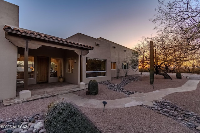 back of house at dusk featuring a patio area and stucco siding