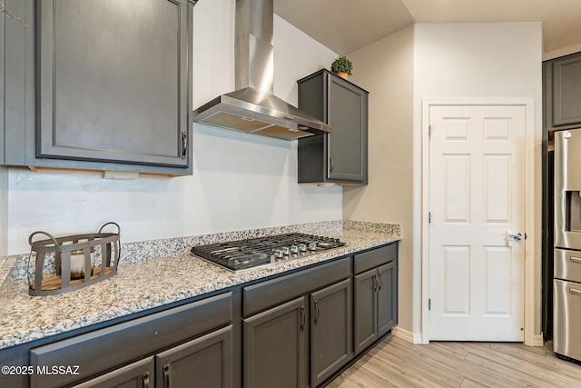 kitchen with light wood-type flooring, light stone countertops, wall chimney exhaust hood, and appliances with stainless steel finishes