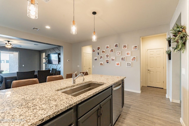 kitchen with sink, light stone counters, light wood-type flooring, stainless steel dishwasher, and pendant lighting