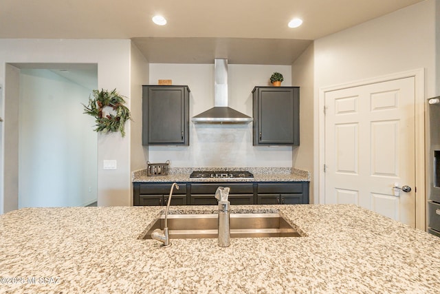 kitchen featuring stainless steel gas cooktop, sink, wall chimney range hood, and light stone counters