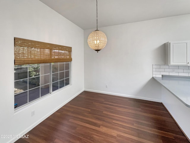 unfurnished dining area featuring an inviting chandelier, dark hardwood / wood-style flooring, and vaulted ceiling