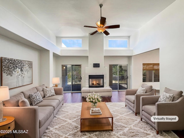 living room featuring wood-type flooring, a tile fireplace, ceiling fan, and a high ceiling