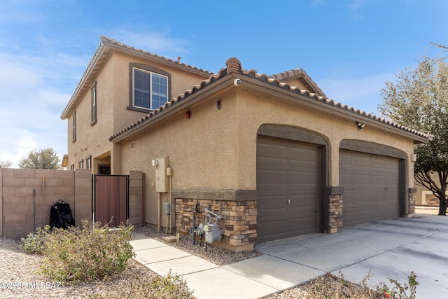 view of side of property featuring an attached garage, fence, stone siding, and stucco siding