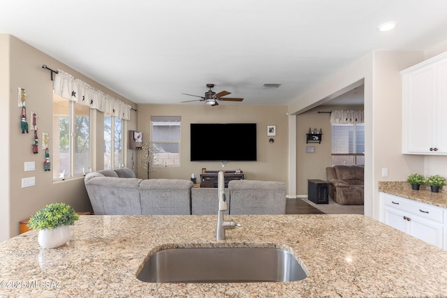 kitchen featuring white cabinetry, light stone countertops, sink, and ceiling fan