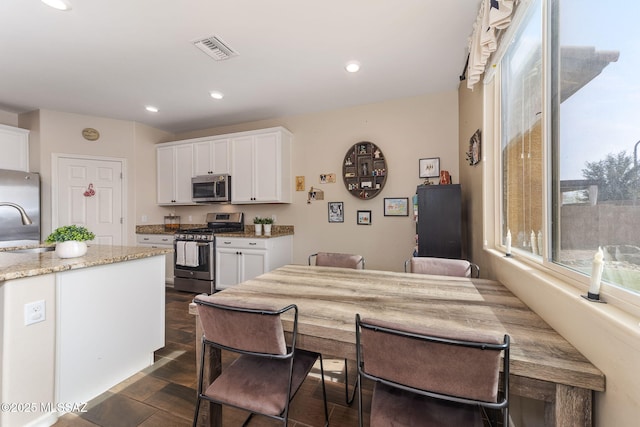 kitchen with white cabinetry, stainless steel appliances, sink, and light stone counters