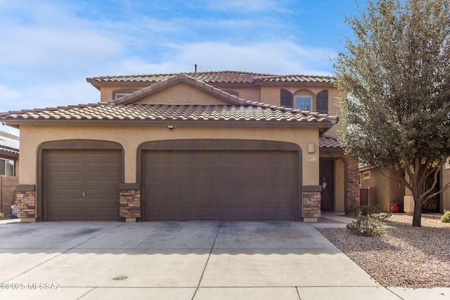 mediterranean / spanish home with concrete driveway, stucco siding, stone siding, an attached garage, and a tile roof
