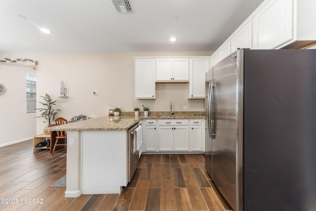 kitchen with sink, appliances with stainless steel finishes, light stone countertops, white cabinets, and kitchen peninsula