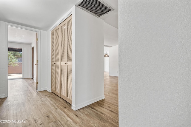 corridor with visible vents, baseboards, a textured wall, and wood finished floors