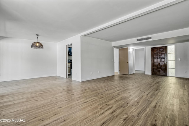 unfurnished living room featuring visible vents, baseboards, and wood finished floors