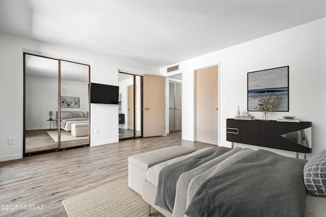 bedroom with two closets, wood finished floors, and visible vents