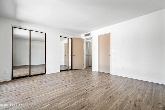 unfurnished bedroom with visible vents, baseboards, multiple closets, and wood finished floors