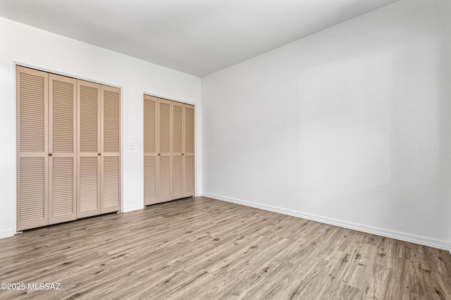 unfurnished bedroom featuring baseboards, two closets, and wood finished floors
