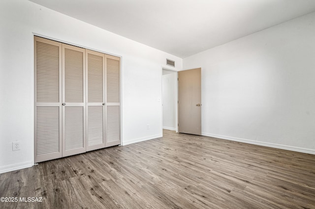 unfurnished bedroom featuring visible vents, baseboards, a closet, and wood finished floors