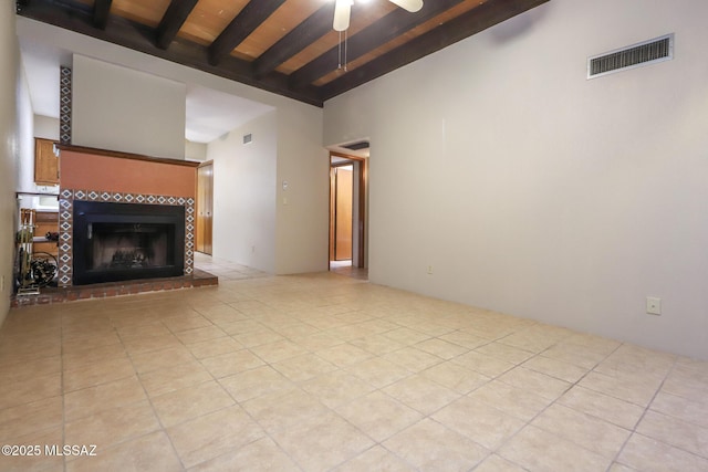 unfurnished living room featuring beamed ceiling, a tiled fireplace, light tile patterned floors, ceiling fan, and wood ceiling