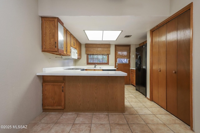 kitchen with sink, light tile patterned floors, kitchen peninsula, and black fridge