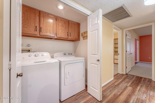 clothes washing area featuring cabinets, separate washer and dryer, light hardwood / wood-style flooring, and a textured ceiling